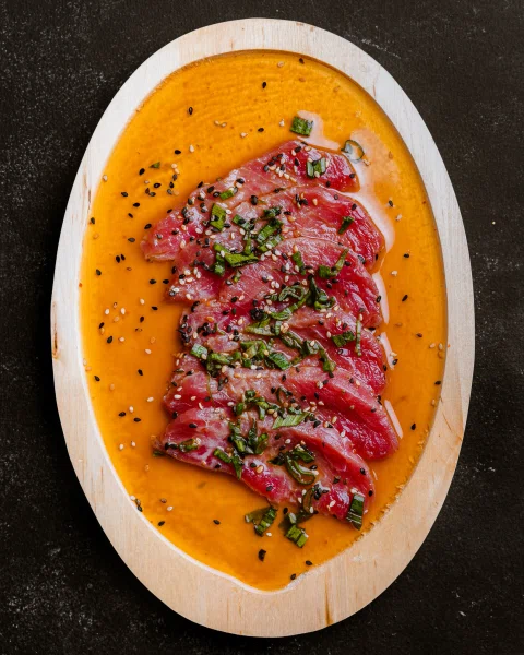 Láminas de pescado crudo sobre salsa naranja en vista cenital.