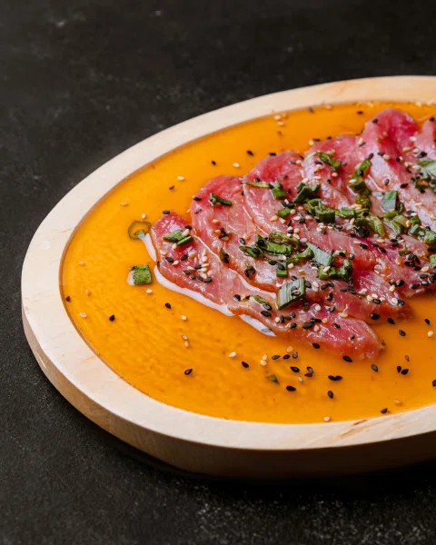 Láminas de pescado crudo sobre salsa naranja.