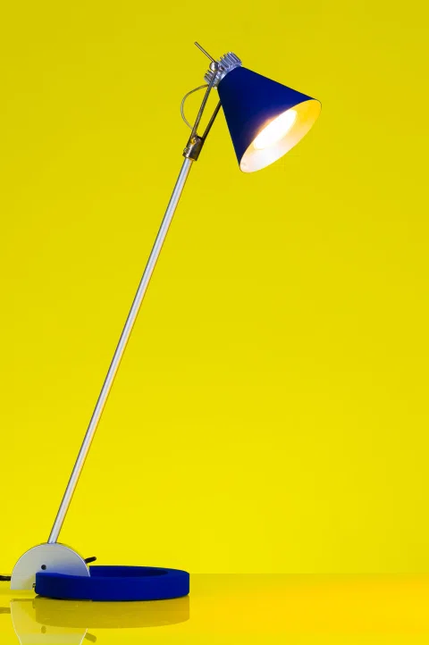 Lámpara de escritorio azul presentada sobre fondo amarillo.