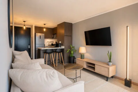Living de departamento con cocina integrada y televisión.