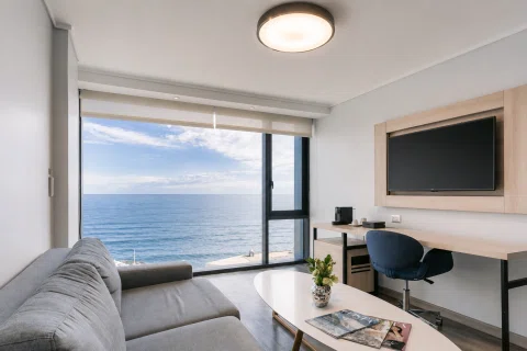 Living de hotel con un gran ventanal y vista al mar.