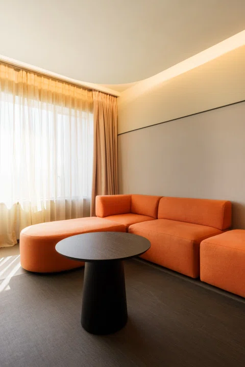 Living de suite con sofá naranja y mesas redondas.