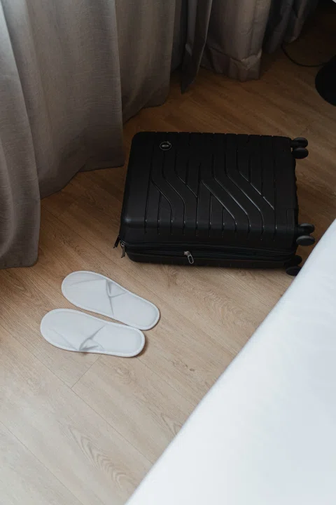 Maleta abierta y pantuflas junto a cama.