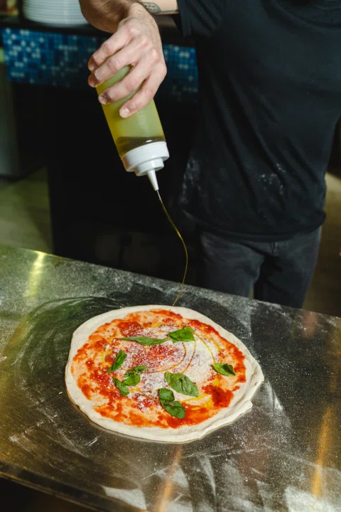 Mano agregando aceite sobre pizza antes del horno.