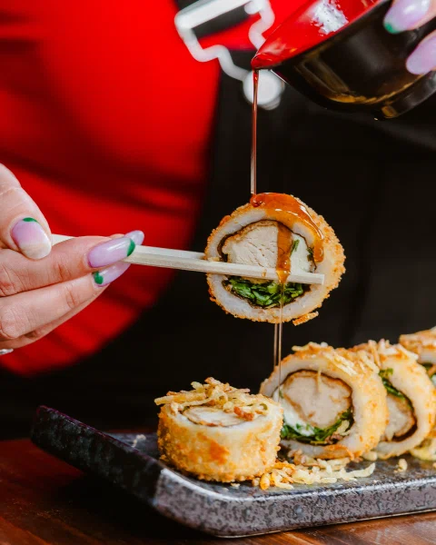 Mano agregando salsa sobre roll de sushi.