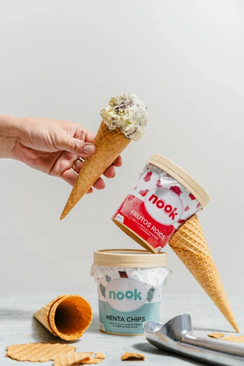 Mano con cono de helado junto a potes Nook apilados.