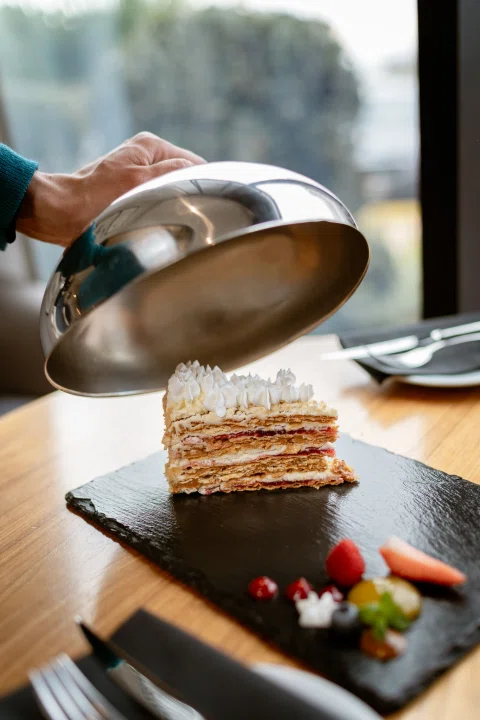 Mano levantando campana metálica sobre postre.