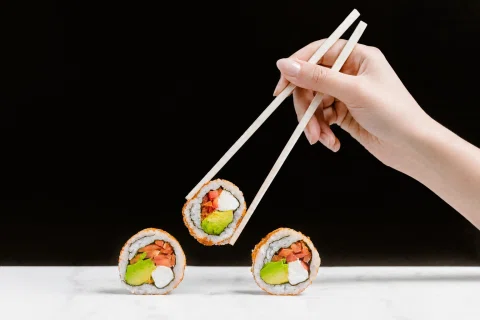 Mano levantando sushi con palillos sobre fondo negro.