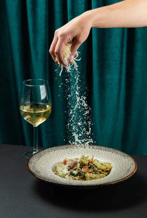 Mano sazonando plato junto a copa de vino.