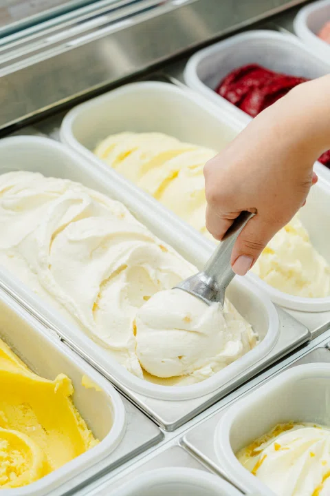 Mano sirviendo helado blanco desde vitrina.