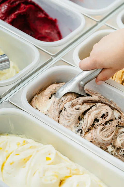 Mano sirviendo helado de cookies desde vitrina.