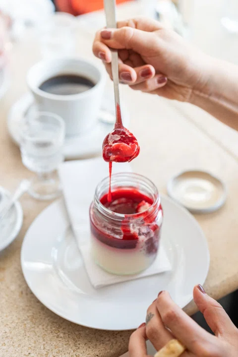 Mano sirviendo salsa roja sobre postre.