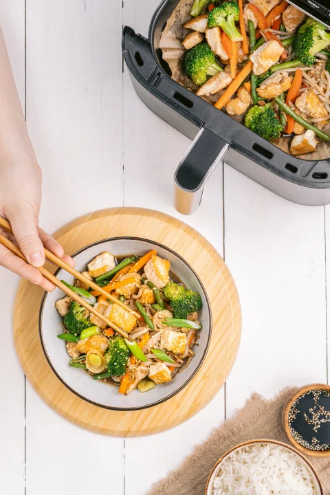 Mano sirviendo vegetales desde air fryer.