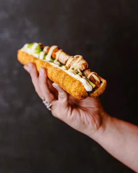 Mano sosteniendo un roll tipo burrito de sushi.