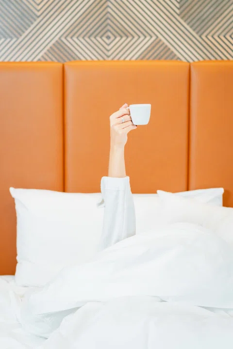 Mano sosteniendo teléfono sobre cama de hotel.