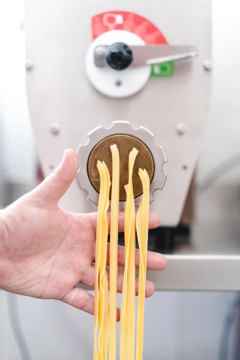 Mano sosteniendo tiras largas de pasta fresca.