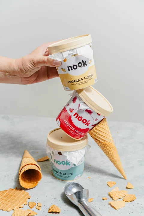 Envases de helado Nook apilados junto a conos y utensilios.