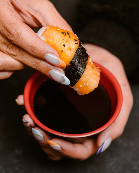 Mano sumergiendo sushi en salsa de soya.