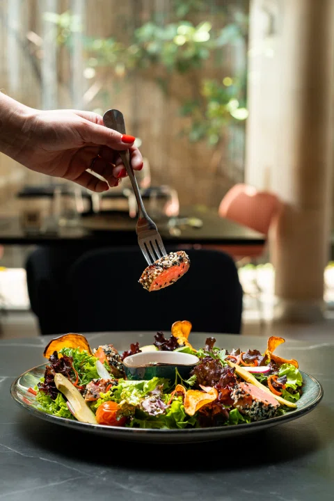 Mano terminando ensalada en plato negro.