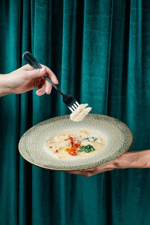 Mano terminando plato con salsa frente a cortina verde.