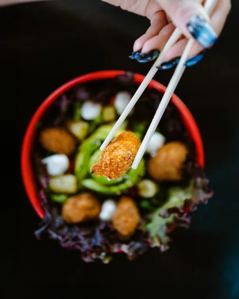 Mano tomando pieza frita desde bowl con palillos.