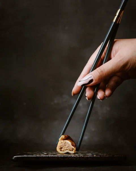 Mano tomando una pieza de sushi con palillos.