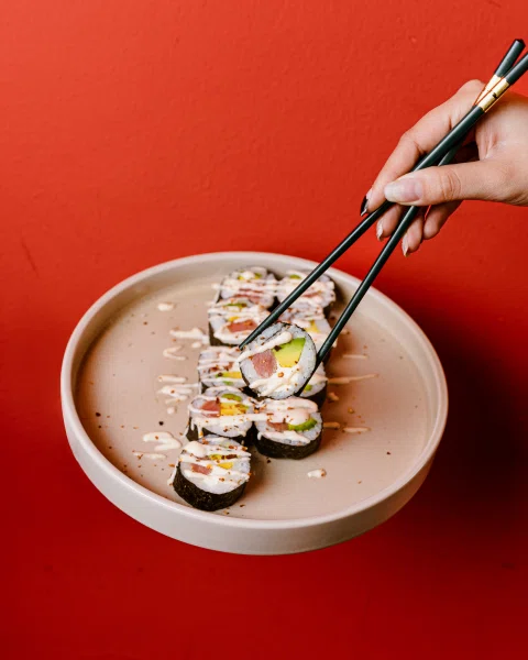 Mano tomando piezas de sushi de un plato.