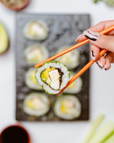 Mano tomando sushi con palillos sobre bandeja.