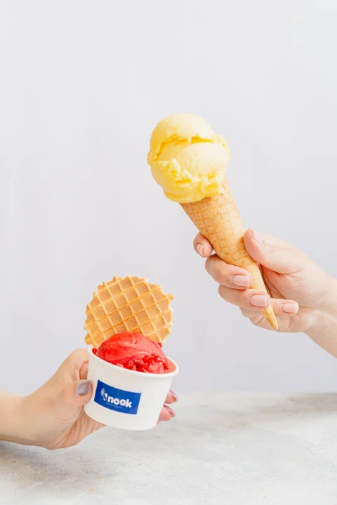 Manos sosteniendo cono y vaso de helado Nook.