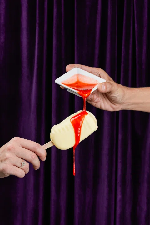 Manos vertiendo salsa roja sobre postre claro.