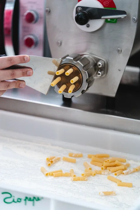 Máquina extruyendo pasta fresca sobre bandeja.