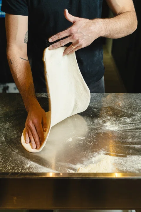 Masa de pizza levantada sobre mesón.