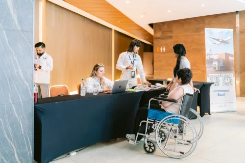 Mesa de registro atiende a una asistente usuaria de silla de ruedas.