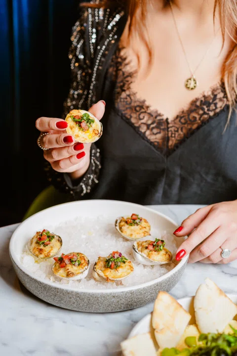 Mujer con cóctel acompañando plato de bocados.