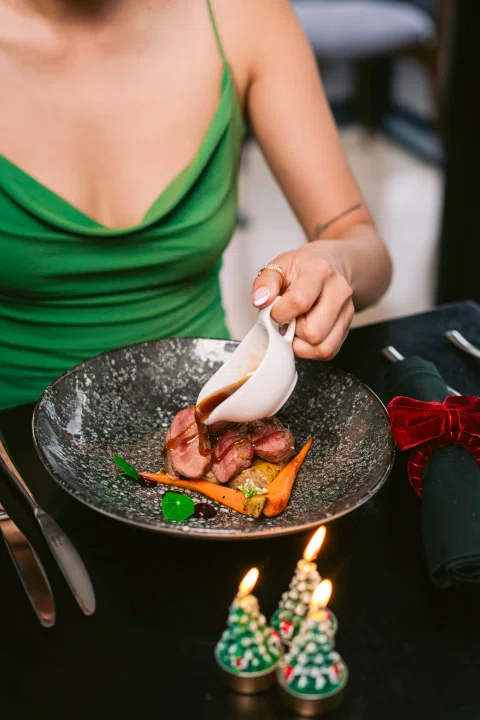 Mujer comiendo plato gastronómico en mesa.