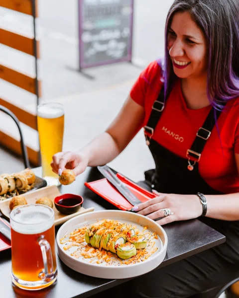 Mujer comiendo sushi acompañada de cerveza.