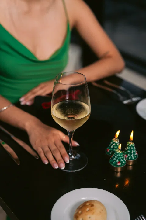 Mujer con copa de vino junto a mesa.