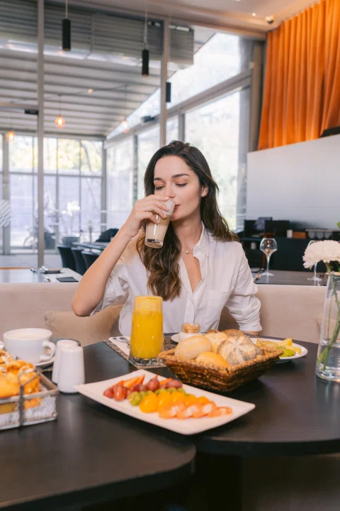 Mujer desayunando con jugo y platos variados.
