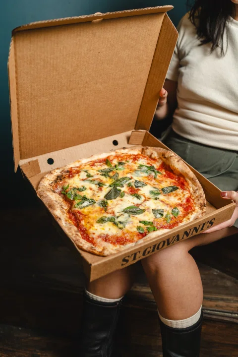 Mujer mostrando pizza dentro de caja abierta.