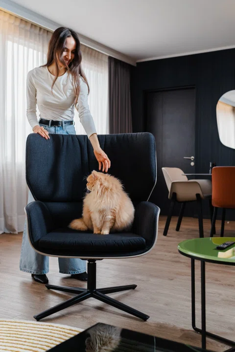 Mujer de pie junto a perro sentado en sillón.