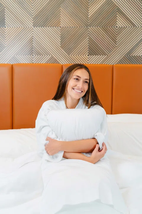 Mujer sentada sobre cama con cabecero naranja.