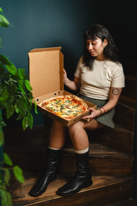 Mujer sentada sosteniendo caja abierta con pizza.