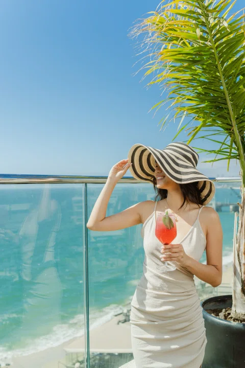 Mujer con sombrero en terraza junto al mar.