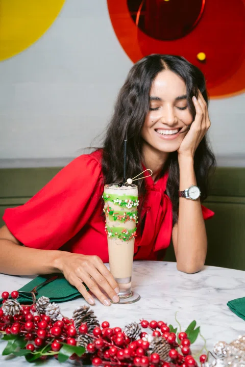 Mujer sonriendo junto a cóctel y decoración festiva.