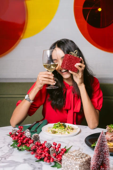 Mujer sosteniendo cóctel y teléfono en mesa festiva.