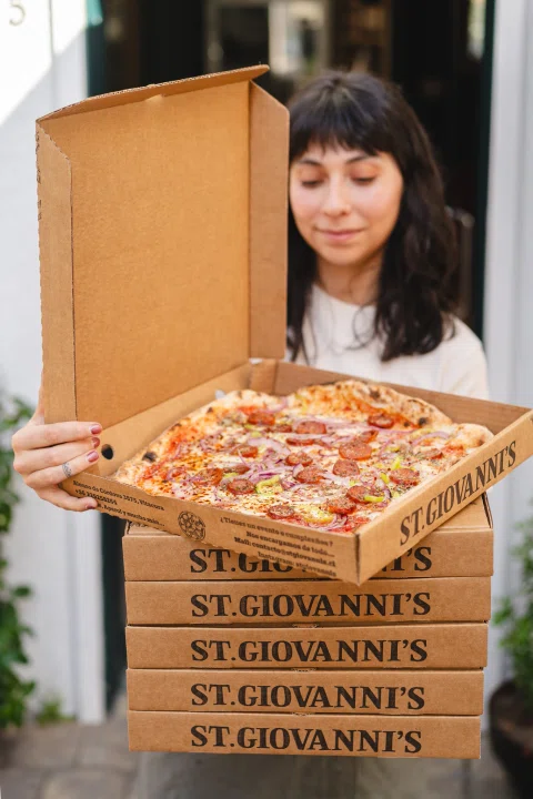 Mujer sosteniendo pizza sobre torre de cajas.