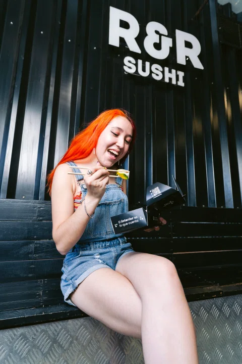 Mujer muestra una pieza de sushi frente a un restaurante.