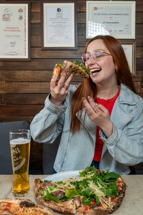 Mujer tomando bebida junto a pizzas sobre mesa.