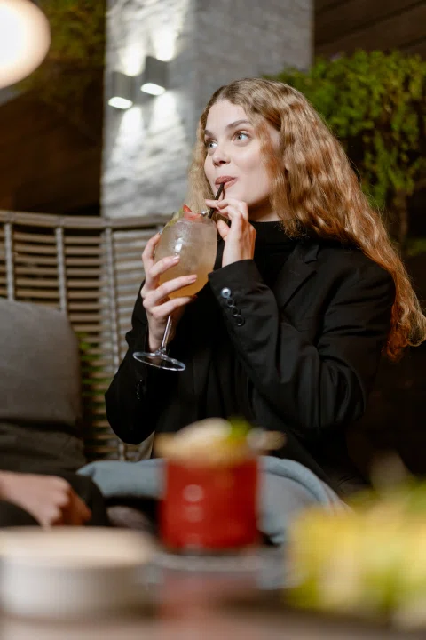 Mujer tomando bebida en terraza nocturna.