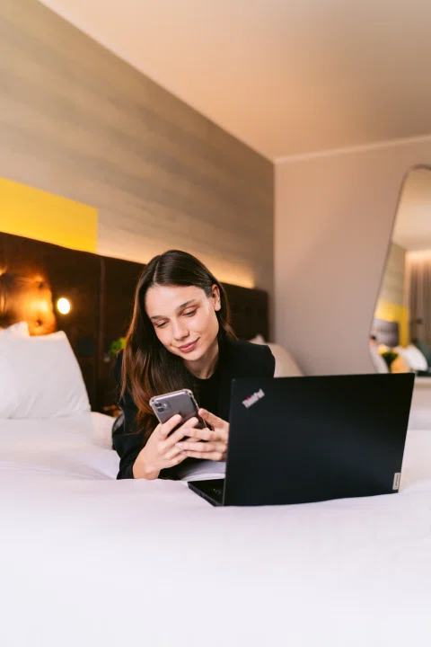 Mujer trabajando con notebook sobre cama de hotel.